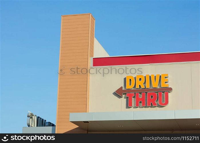 Drive thru sign with left arrow on building against the blue clear sky. Copy space wallpaper.