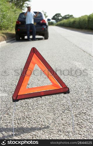 Driver Broken Down On Country Road With Hazard Warning Sign In Foreground