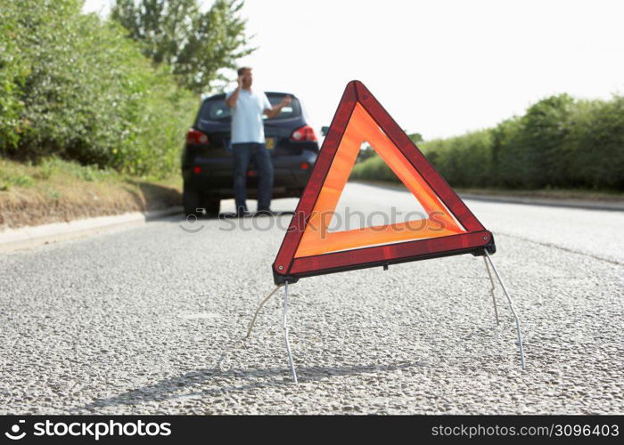 Driver Broken Down On Country Road With Hazard Warning Sign In Foreground