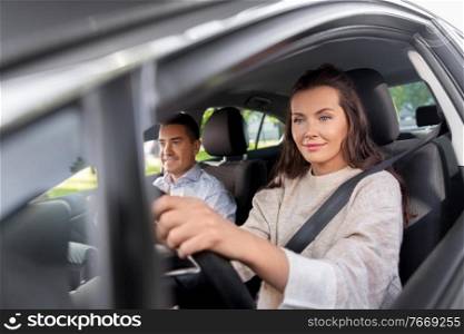 driver courses and people concept - young woman learning to drive car with driving school instructor. woman and driving school instructor in car