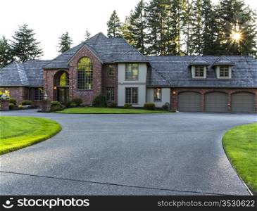 Driveway to large brick and cedar home with trees and sunlight in background