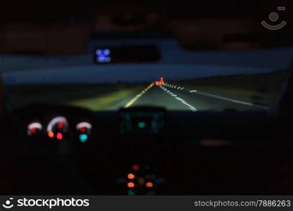Driving a car at night. View from inside with luminous dashboard and blurry lights of the road