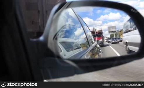 Driving a car in city with view from side mirror.