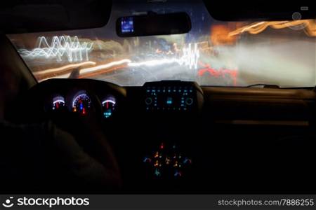 Driving a car in the city at night. Traveling on high speed, road lights defocused. View from inside with luminous dashboard