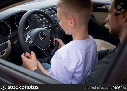 Driving instructor, driving school, child driving, dad and son, long trip, hold the steering wheel, car device, family day. Dad and a cute boy hold the steering wheel of a car with their hands