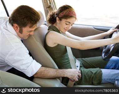 Driving instructor or father encouraging a teen driver to use her seatbelt.