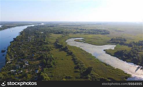 Drone fly over waving river of blue color surrounded by local village with various buildings and Wetland and marsh habitat with a reedbed of Common Reed aerial view. Top view.