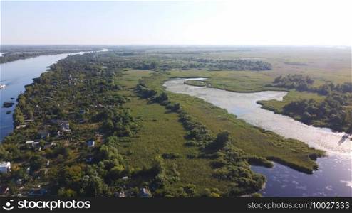 Drone fly over waving river surrounded by local village with various buildings and Wetland and marsh habitat with a reedbed of Common Reed aerial view. Top view.