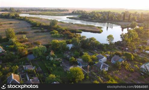 Drone fly over waving river surrounded by local village with various buildings and Wetland and marsh habitat with a reedbed of Common Reed aerial view. Top view.