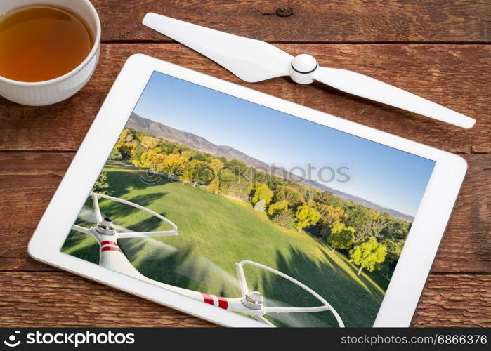 drone flying over park in fall colors - reviewing aerial image on a digital tablet with a cup of tea