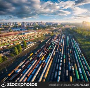 Drone view of freight trains at sunset. Colorful railway cargo wagons on railroad. Aerial view of colorful wagons, city, blue sky with clouds. Depot of freight trains. Railway station. Transportation