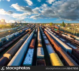 Drone view of freight trains at sunset. Colorful railway cargo wagons on railroad. Aerial view of colorful wagons, city, blue sky with clouds. Depot of freight trains. Railway station. Transportation. Drone view of freight trains at sunset. Railway cargo wagons