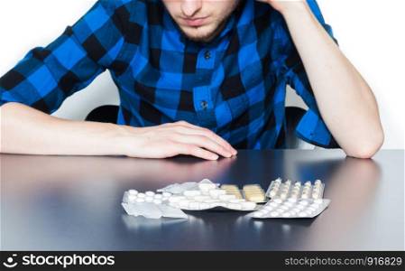 Drug abuse: Young man sitting on a table, drugs and pills in front of him