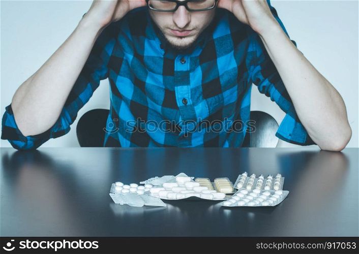 Drug abuse: Young man sitting on a table, drugs and pills in front of him