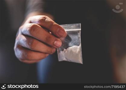 Drug dealer selling junkie. Man hand holds plastic packet or bag with addict narcotics cocaine powder or another, drug dealer sale and danger addiction overdose concept.
