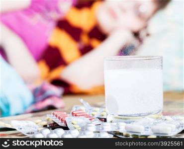 drug dissolves in water and pills on table close up and sick woman with scarf around her neck on sofa in living room on background