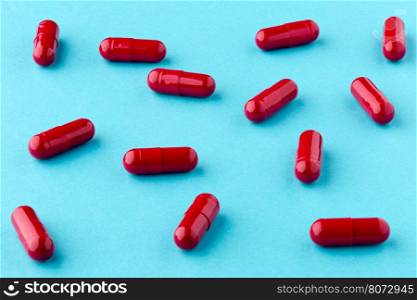 Drug red capsules scattered on the blue background. Medicinal red capsules scattered on the table on the blue background