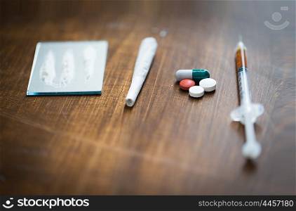 drug use, crime, addiction and substance abuse concept - close up of crack cocaine drug dose track on mirror with marijuana joint, pills and syringe