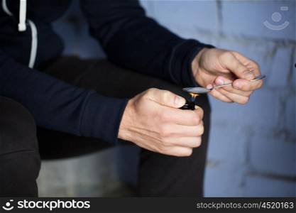 drug use, crime, addiction, substance abuse and people concept - close up of addict with lighter and spoon preparing dose of crack cocaine on street