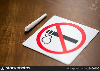 drug use, substance abuse, addiction and no smoking concept - close up of marijuana joint or handmade cigarette with prohibiting sign
