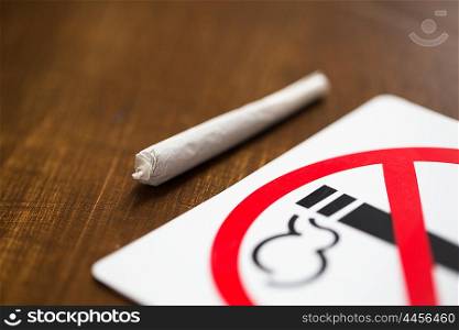 drug use, substance abuse, addiction and no smoking concept - close up of marijuana joint or handmade cigarette with prohibiting sign