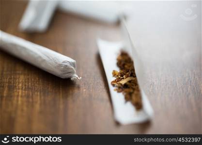 drug use, substance abuse, nicotine addiction and smoking concept - close up of marijuana joint and tobacco
