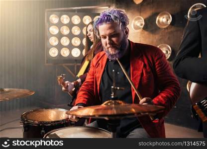 Drummer in red suit on the stage with lights, bas-guitarist on background. Rock band concert, music show