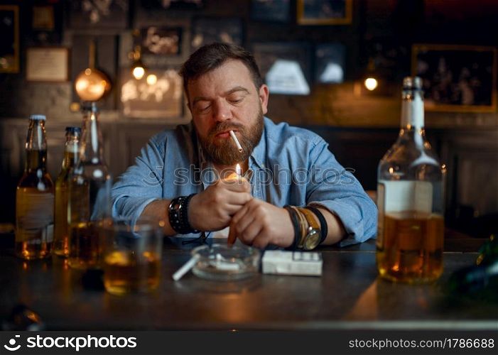 Drunk man smokes a cigarette at the counter in bar. One male person resting in pub, human emotions and leisure activities, depression, stress relief. Drunk man smokes a cigarette at the counter in bar