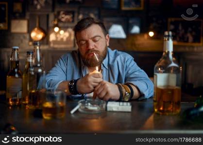 Drunk man smokes a cigarette at the counter in bar. One male person resting in pub, human emotions and leisure activities, depression, stress relief. Drunk man smokes a cigarette at the counter in bar