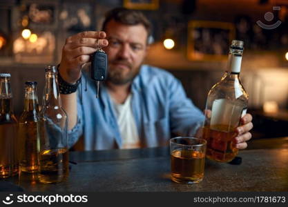 Drunk man with car key sitting at the counter in bar. One male person resting in pub, human emotions and leisure activities. A reasonable act, refuses to drive under the influence of alcohol. Drunk man with car key sitting at counter in bar