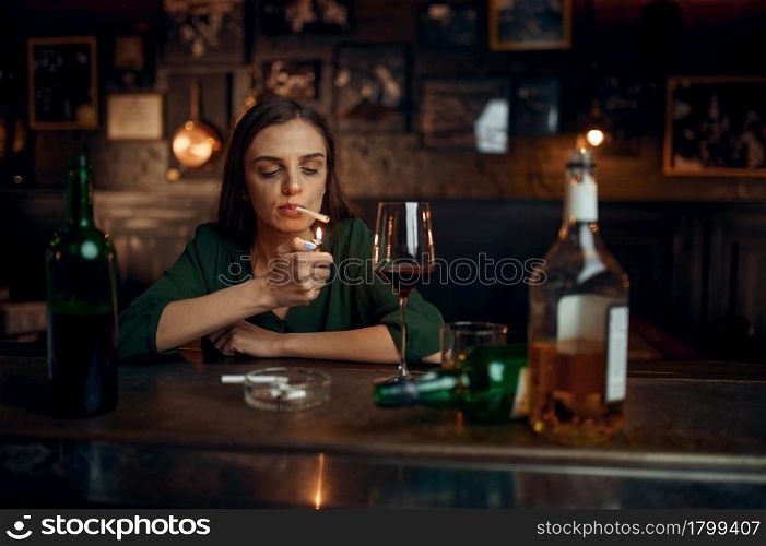 Drunk woman smokes a cigarette at the counter in bar. One female person in pub, human emotions, leisure activities, depression. Drunk woman smokes a cigarette at counter in bar