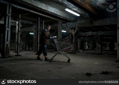 Drunk young homeless woman pushing shopping trolley cart with her belongings at night in old abandoned building. Drunk young homeless woman pushing shopping trolley cart