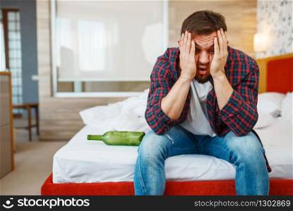 Drunken man awake in bed with bottle of wine. Male person with alcohol hangover, headache and depression, bad morning. Drunken man awake in bed with bottle of wine