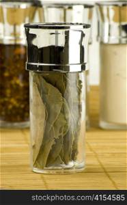 dry bay leaves in a glass jar on different spices background over wooden mat