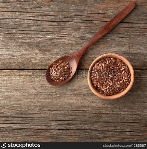 dry brown flax seeds in a brown wooden spoon on a gray wooden table from old boards, top view