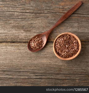 dry brown flax seeds in a brown wooden spoon on a gray wooden table from old boards, top view