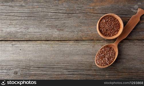 dry brown flax seeds in a brown wooden spoon on a gray wooden table from old boards, top view