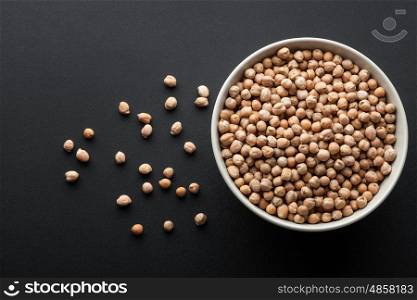 dry chickpeas in white bowl isolated on dark background. top view