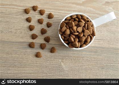 Dry dog food in a white mug isolated on a wooden background