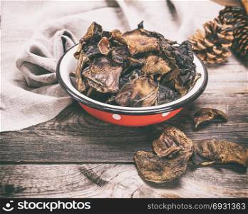 dry forest mushrooms in an iron red plate on a gray wooden background