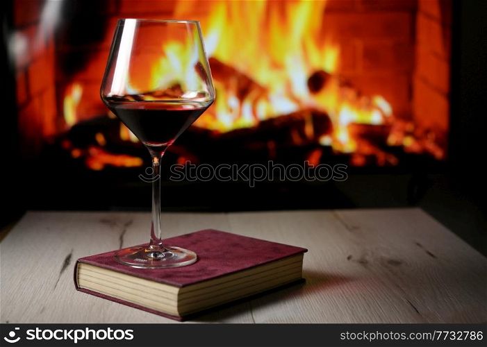 Dry Glass Of Red Wine on Book and Fireplace in Background