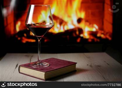 Dry Glass Of Red Wine on Book and Fireplace in Background