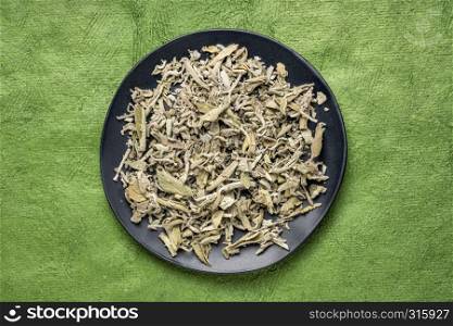dry Greek sage herb tea (fascomilo) on a black plate against green textured bark paper