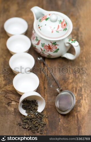 dry green chinese tea set,with strainer closeup,cups and teapot on background over old wood board