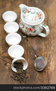 dry green chinese tea set,with strainer closeup,cups and teapot on background over old wood board