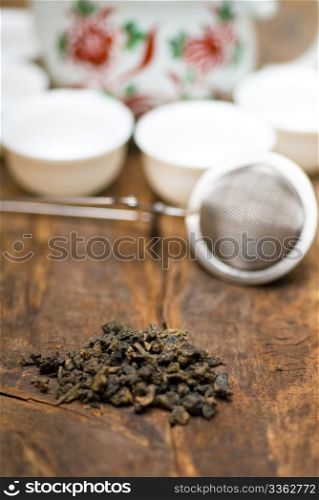 dry green chinese tea set,with strainer closeup,cups and teapot on background over old wood board