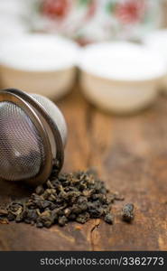 dry green chinese tea set,with strainer closeup,cups and teapot on background over old wood board