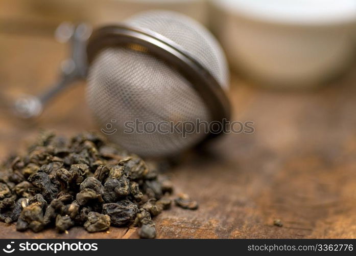 dry green chinese tea set,with strainer closeup,cups and teapot on background over old wood board