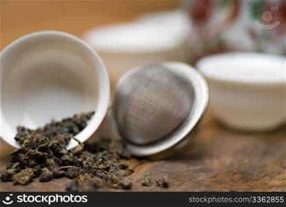 dry green chinese tea set,with strainer closeup,cups and teapot on background over old wood board