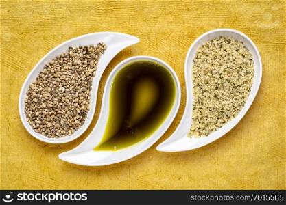 dry hemp seeds, hearts and oil in small teardrop bowls against red textured paper